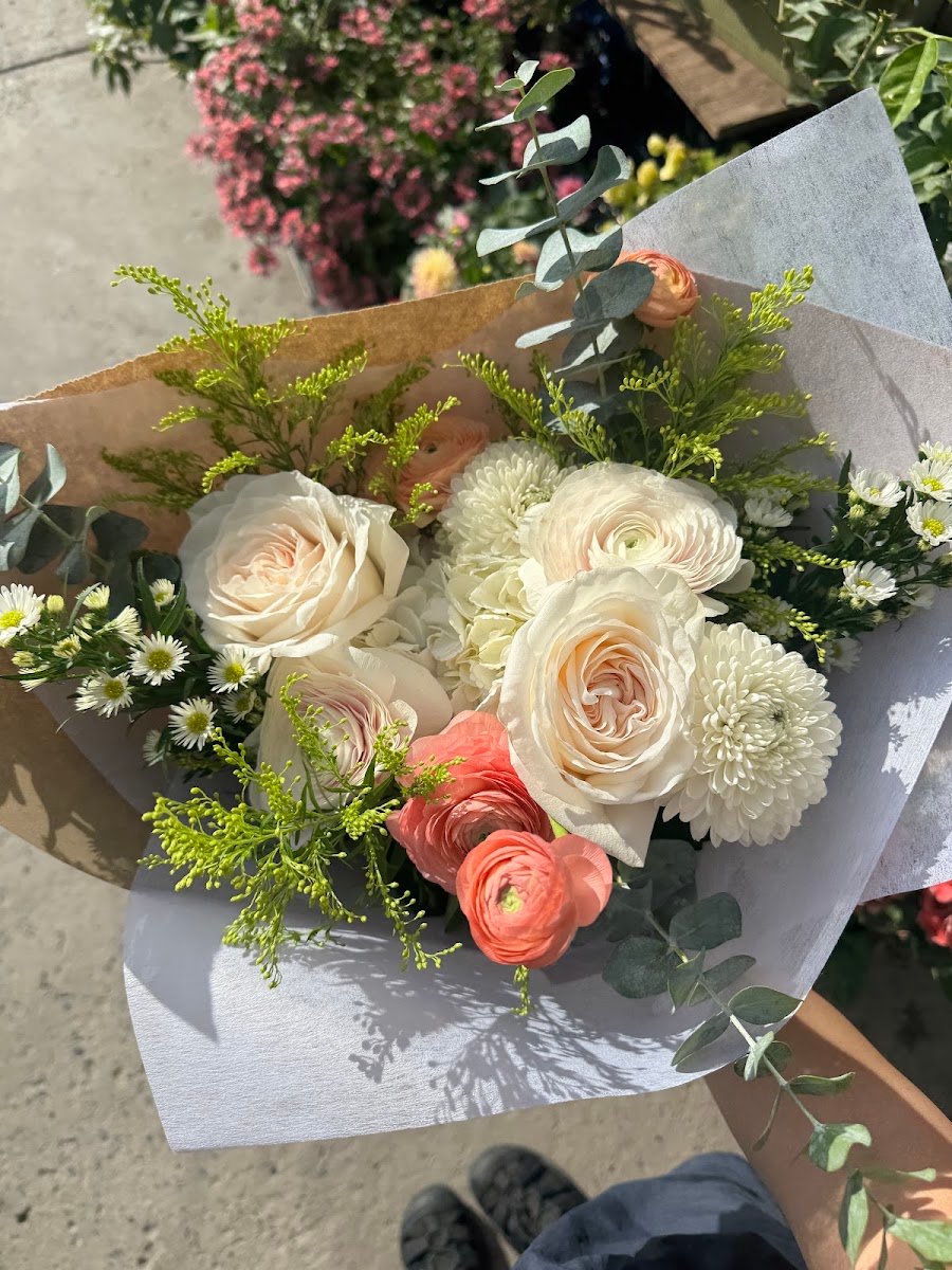Bouquet fait main aux tons crème, pêche et vert, enveloppé de papier.