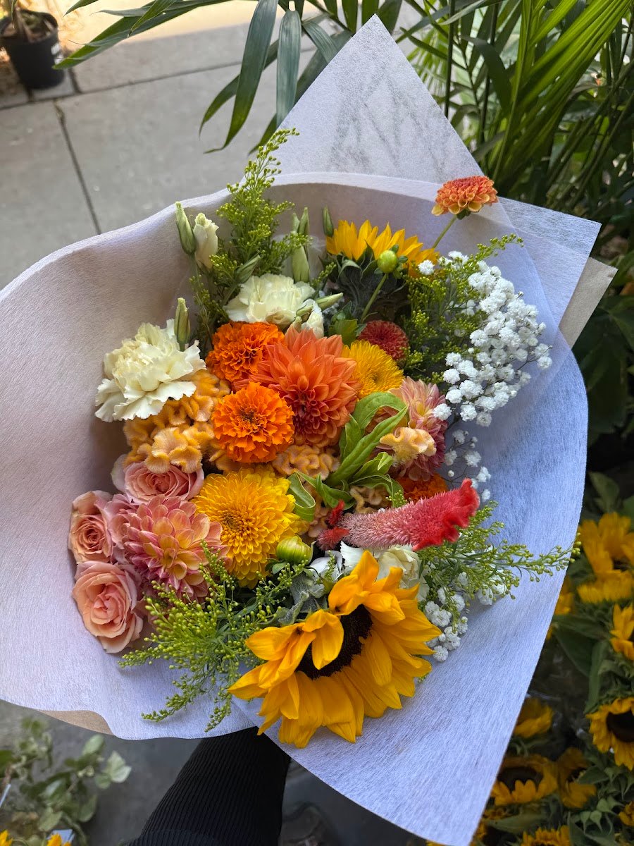 Bouquet aux tons d'automne : tournesols, dahlias et roses, enveloppé de papier.